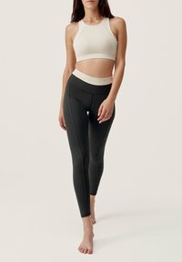 Beige sportbeha met een hoge hals en zwarte high-waisted legging met contrasterende naden en een gladde textuur.