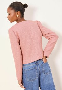 Veste rose texturée à manches longues et coupe courte, associée à un jean en denim bleu taille haute avec des poches arrière.
