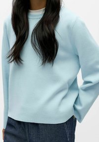 Jasnoniebieska bluza z okrągłym dekoltem, miękka w dotyku, z długimi rękawami. W połączeniu z ciemnymi dżinsami ma luźny, casualowy fason.