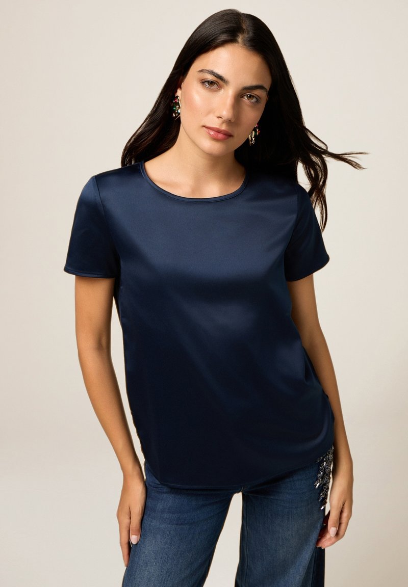 Maglietta blu navy a maniche corte con scollatura rotonda, realizzata in materiale liscio, indossata con jeans blu con dettagli decorativi.