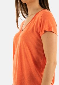 T-shirt orange à col en V en tissu doux, avec des manches courtes et une coupe décontractée. Texture remarquable qui ajoute un look décontracté.