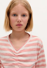 Rosa und weiße gestreifte V-Ausschnitt-Bluse mit gerafftem Detail an der Vorderseite; weicher Stoff mit glatter Textur, kurze Ärmel.