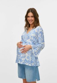 Blusa a maniche lunghe blu chiaro con motivi a foglia, scollo a V e cintura legata in vita, abbinata a pantaloni shorts in denim. Texture liscia.