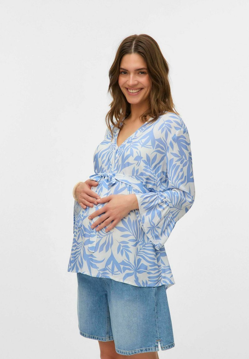 Blusa a maniche lunghe blu chiaro con motivi a foglia, scollo a V e cintura legata in vita, abbinata a pantaloni shorts in denim. Texture liscia.