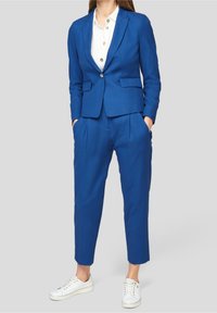 Blå skräddarsydd kavaj och matchande byxor i slätt tyg, med en figurnära design, sidofickor och vita sneakers.