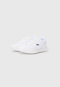 Baltos žemių sneakersai su tekstūruota pade ir žaliu krokodilo logotipu šone, šiek tiek pasvirę į dešinę ant vientiso fono.