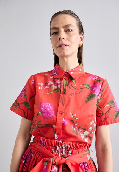 Red floral shirt with short sleeves, featuring pink and green botanical patterns. Button closure and collar detail, made from lightweight fabric.