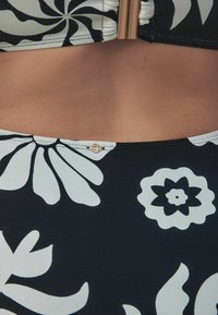 Haut de bikini floral noir et blanc avec un tissu texturé, des motifs audacieux et un accent en métal doré près du col.