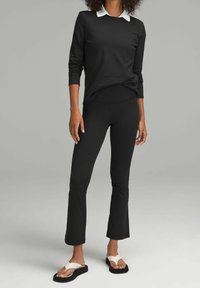 Czarna bluzka z długim rękawem i białym kołnierzykiem, zestawiona z dopasowanymi czarnymi spodniami i białymi sandałami wsuwanymi, posiadającymi płaską podeszwę i prosty design.