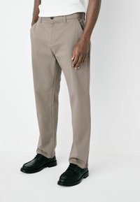 Beige chinos with a straight-leg design, crafted from cotton blend fabric. Features front pockets and a single button closure, paired with black shoes.