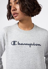 Grijze sweatshirt gemaakt van zachte stof met een navy "Champion" logo. Ronde halslijn en lange mouwen maken het ontwerp compleet.