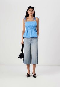 Light blue peplum top with adjustable tie straps, paired with light denim culottes. Black handbag and pointed-toe shoes complete the outfit.