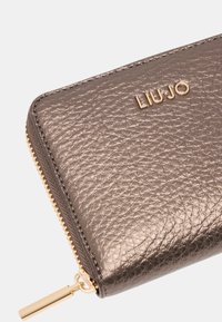 Portafoglio grigio metallizzato realizzato in pelle texturizzata, con una cerniera d'oro e un logo impresso in oro. Forma rettangolare compatta con accenti lisci.