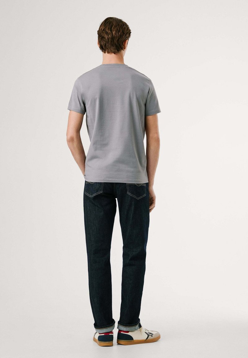 Graues T-Shirt mit kurzen Ärmeln und Rundhalsausschnitt, kombiniert mit dunkelblauen Jeans und weißen Sneakern mit farblichen Akzenten.