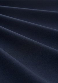 Marinblått tyg med en slät, matt yta, som har subtila draperingar och veck, vilket skapar djup och visuell intresse.