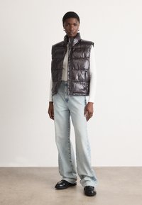 Padded bezrukavna jakna tamnosmeđe boje, sjajnog materijala s visokim ovratnikom. Uparena s svijetloplavim trapeznim farmerkama i crnim platformskim cipelama.