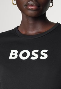 Černé tričko s kulatým výstřihem, které na přední straně nese výrazný bílý nápis "BOSS". Hladká bavlněná látka.