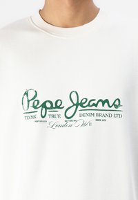 Sudadera blanca con texto impreso en verde. El diseño incluye "Pepe Jeans" y detalles adicionales de marca en una fuente casual.