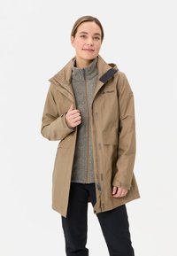 Beige waterdichte jas met een rits en capuchon, voorzien van twee voorzakken en een grijze fleece binnenlaag. Logo op de borst.
