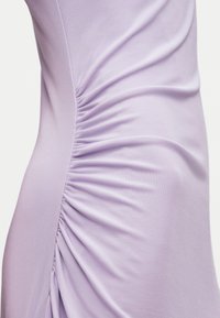 Gros plan sur une robe en tissu lavande avec un détail froncé plissé le long de la couture latérale.