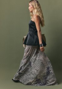 Juoda peplumo tipo palaidinė, tekstūruota, derinama su ilga, plazdančia sijonu smėlio spalvos su juodomis dėmėmis. Juodi batai ir rankinė užbaigia aprangą.