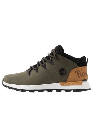 Średniobut oliwkowo-czarny z beżową łatką na pięcie, czarnymi sznurówkami, białą podeszwą i logo Timberland po boku.