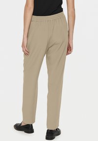 Pantalons beige clair avec une coupe décontractée, dotés d'une taille élastique et de jambes droites, associés à des chaussures noires à enfiler.