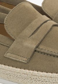 Zielony zamszowy but wsuwany z detalem w postaci kokardy, z teksturowaną, plecioną podeszwą i kontrastującymi szwami. Zbliżenie podkreślające materiał i wzornictwo.
