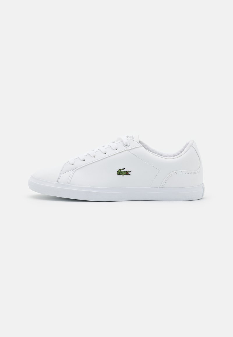 Sneaker bianco realizzato in materiale sintetico con texture liscia, caratterizzato da un logo verde ricamato sul lato e un motivo cucito discreto.