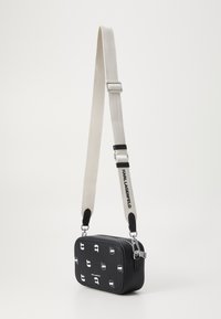 Black faux leather bag with white graphic designs, rectangular shape, silver hardware, and a detachable beige strap with logo.
