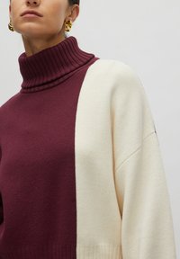 Bordeaux-rot und cremefarbener Rollkragenpullover mit geripptem Kragen und Ärmeln, im oversized Schnitt und mit glatter Textur.