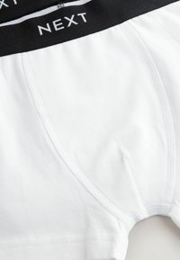 Boxers en coton blanc avec une ceinture élastique noire portant le logo "NEXT", texture lisse et détails de couture renforcée.