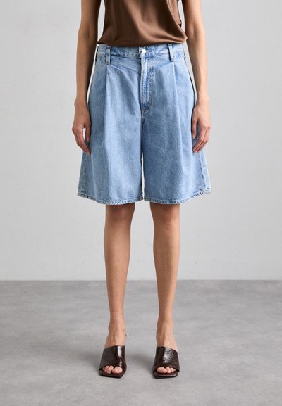 Helle blaue Denim-Bermudashorts mit hoher Taille, Falten und rohem Saum. Kombiniert mit dunkelbraunen offenen Mules.