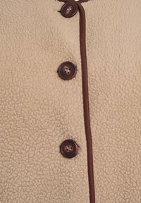 Beige fleecejakke med en tekstureret overflade, brun piping langs kanterne og to mørkebrunne knapper foran.