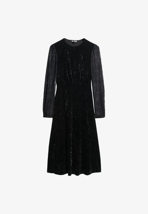 Zwarte fluwelen jurk met lange kanten mouwen, ronde halslijn en een aansluitende lijfje die overgaat in een uitlopende rok. Gelaagd stof met glans.