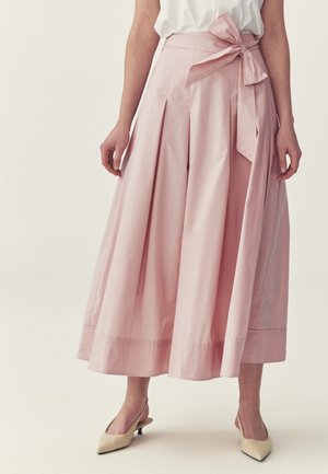 Woman wearing high-waist, wide-leg pink culottes with a large side bow, paired with a white top and beige pointed-toe kitten heels.