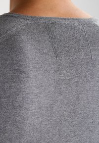 Pull gris en maille avec une texture douce, présentant un détail en patch rectangulaire au niveau de l'encolure arrière et un col rond.