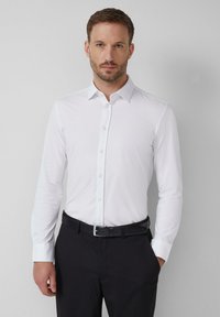 Weißes, langärmliges Hemd mit klassischem Kragen und Knopfleiste. Kombiniert mit schwarzen Hosen und einem schwarzen Gürtel mit silberner Schnalle.