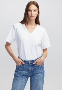 Witte katoenen t-shirt met een V-hals en korte mouwen, met gestikte accenten op de schouders. Gecombineerd met blauwe versierde denim jeans.