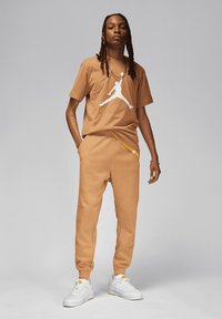 Felpa e pantaloni color sabbia realizzati in tessuto morbido, con il logo Jumpman bianco. Abbinati a scarpe da ginnastica bianche con dettagli gialli.