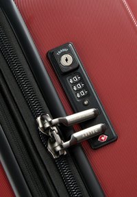 Acercamiento de una maleta roja con un candado de combinación aprobado por la TSA y dos tiradores de cremallera plateados asegurados entre sí.