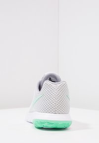 Zapatilla deportiva gris con parte superior de malla texturizada, detalles en verde menta, puntera redondeada y suela con patrón. Presenta un collar y lengüeta acolchados.