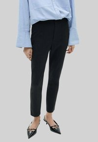 Pantalons noirs slim en tissu lisse, avec une taille mi-haute et une coupe cheville, associés à des talons noirs pointus.