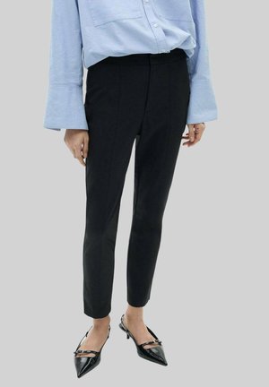 Pantaloni neri slim-fit con una texture liscia, caratterizzati da una vita a media altezza e un taglio alla caviglia, abbinati a tacchi a spillo neri.