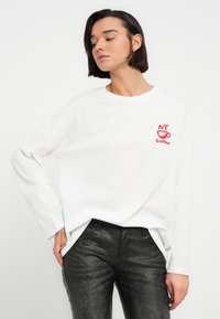 Λευκό μακρυμάνικο μπλουζάκι με κόκκινο σχέδιο "NY coffee" στο στήθος, συνδυασμένο με μαύρο παντελόνι με υφή.