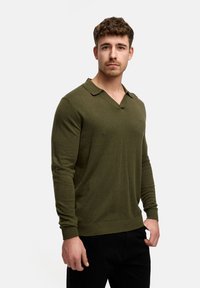 Langærmet olivengrøn polo sweater med V-hals og ribbede manchetter. Har et subtilt logo på brystet og en blød strikket tekstur.