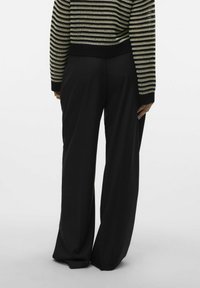 Pantalons larges noirs avec une texture lisse, associés à un pull court avec des rayures horizontales noires et crème.