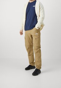 Beige cargo pants with zippered pockets, paired with a navy t-shirt and a cream fleece jacket. Black hiking shoes complete the outfit.