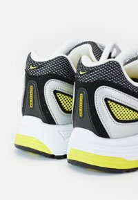 Ténis de corrida pretos, cinzentos e brancos com realces amarelos. Apresentam um upper em malha e uma gola almofadada. Notável marca "Air Pegasus" presente.