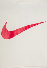 Sudadera blanca cortada hecha de tela suave con un prominente logo de Nike en rojo con un acabado satinado liso.